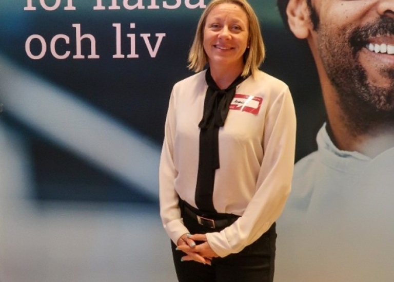 Woman with name tag standing in front of large picture with logo for "Octapharma".