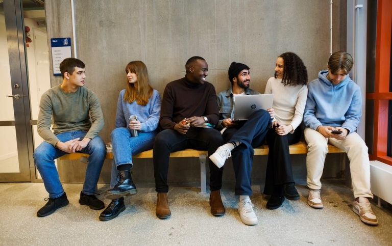 A group of students sitting on a bench indoors, chatting. 