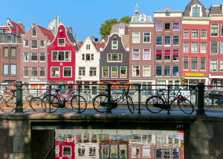 Färgglada byggnader reflekterade i vatten och en bro med parkerade cyklar