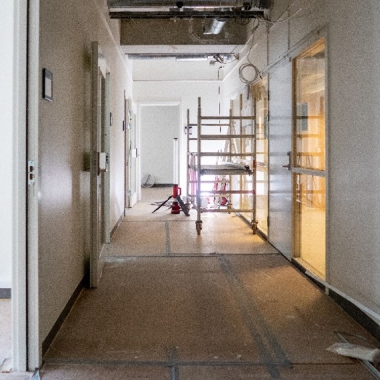 Korridor där det pågår renovering, skyddspapper på golvet, byggställning och sladdar som hänger.