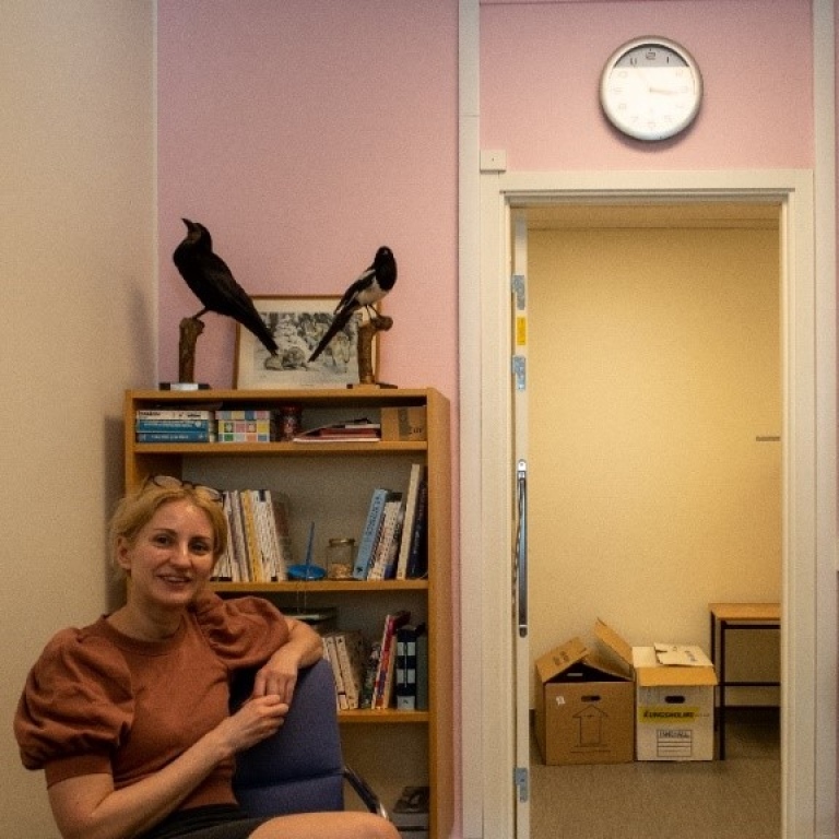 Smiling woman infront of book case in room with pink wall.