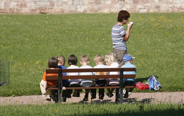 Förskolebarn sitter på en bänk med sin lärare