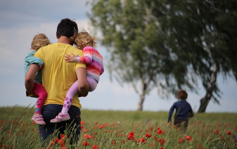 En pappa bär två barn över ett fält