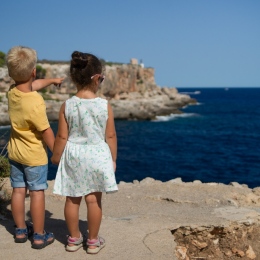 Two children standing near cliff watching on ocean at daytime