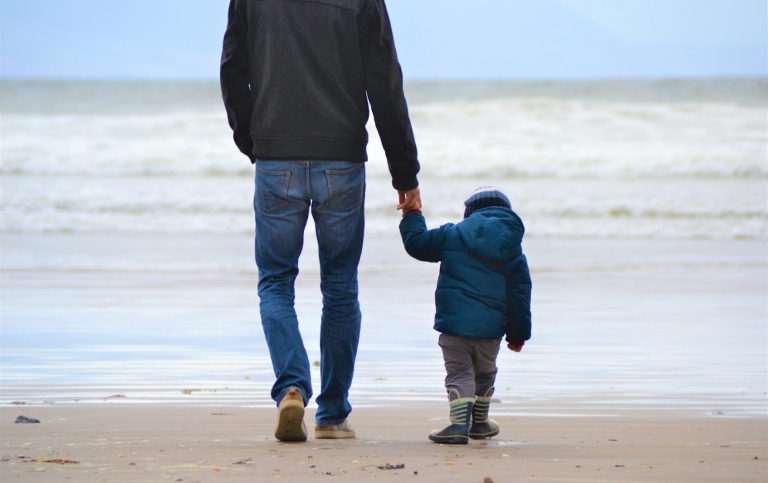 En pappa och hans barn går hand i hand på stranden