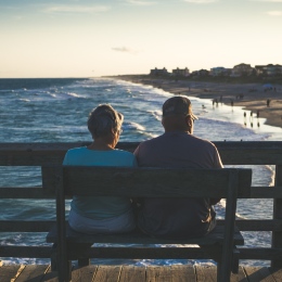 Ett äldre par sitter på en bänk ovanför en strand