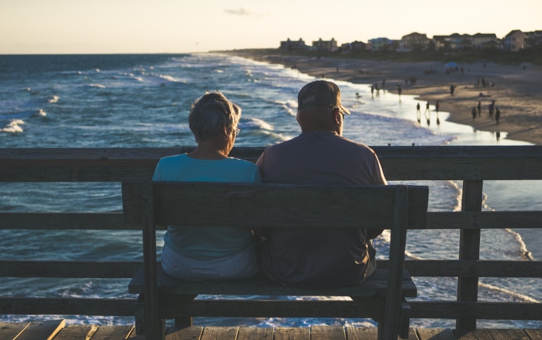 Ett äldre par sitter på en bänk ovanför en strand