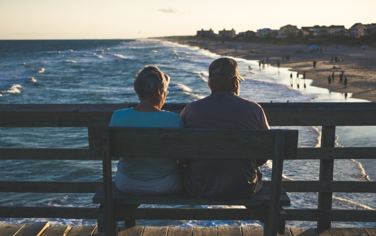 Man and woman sitting on bench in front of beach