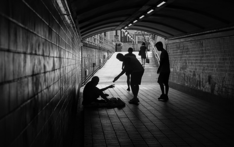 person ger pengar till en tiggare i en tunnel