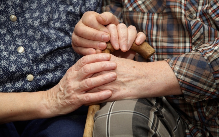 Närbild på gammalt par med käpp som håller varandras händer