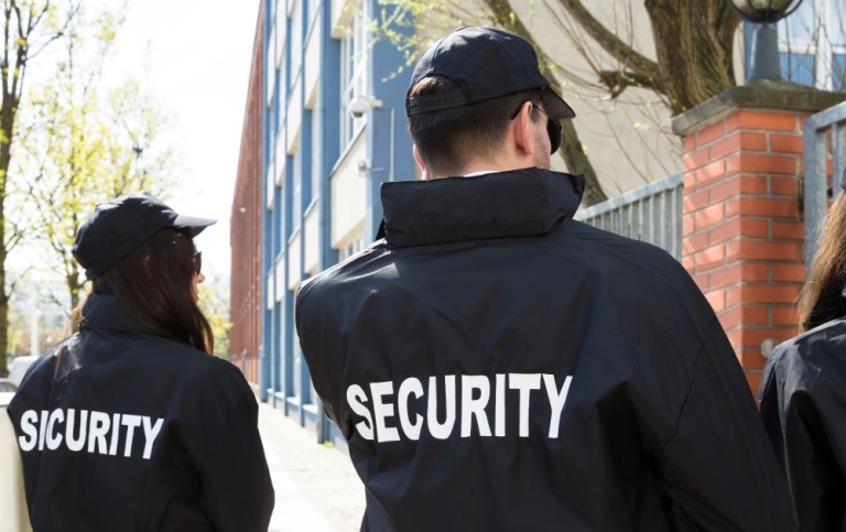 Security guards with jackets standing outside a buildning.