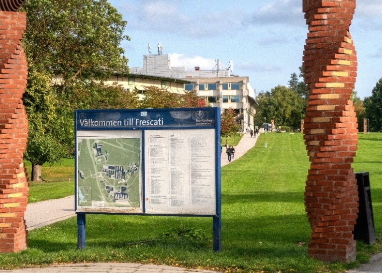 The entrance to Stockholm university campus, including a lawn, building in the background and a sign