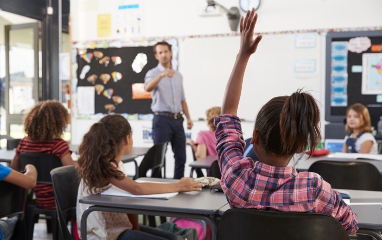 Vy över klassrum med barn som räcker upp händerna