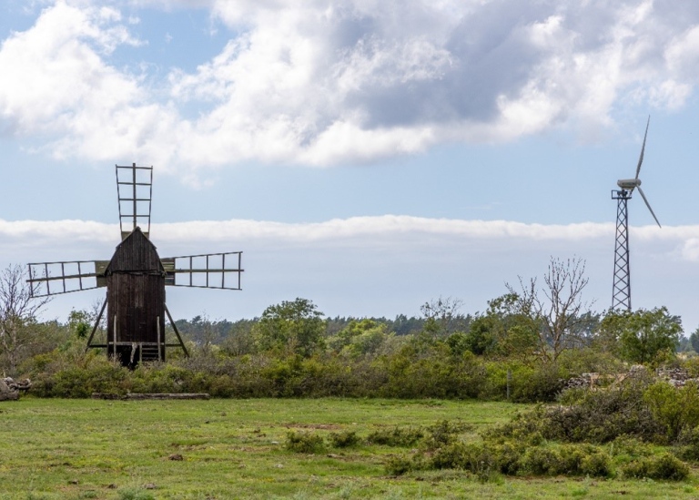 En landskapsbild med en gammal vindkvarn till väntser och ett vindkraftverk till höger.