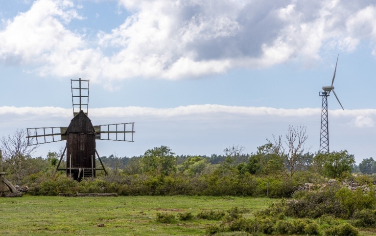 En landskapsbild med en gammal vindkvarn till väntser och ett vindkraftverk till höger.