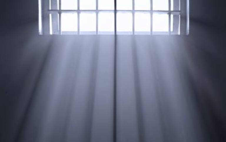 Fängelsegaller i mörker med solljus genom gallret.