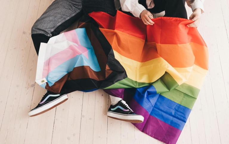 Two people unfolding an LGBTQIA+ flag. Photo from Pexels