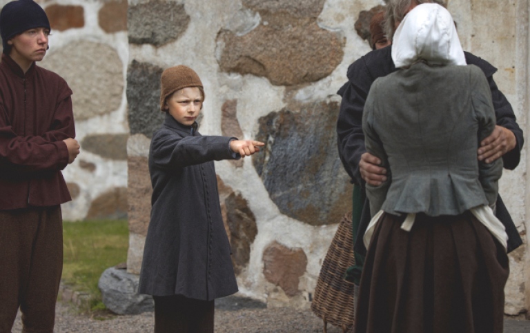 En pojke i 1600-talskläder pekar på en kvinna. 