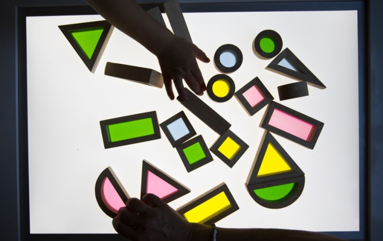 Childrens' hands playing with neon coloured geometrical puzzle pieces on a light board
