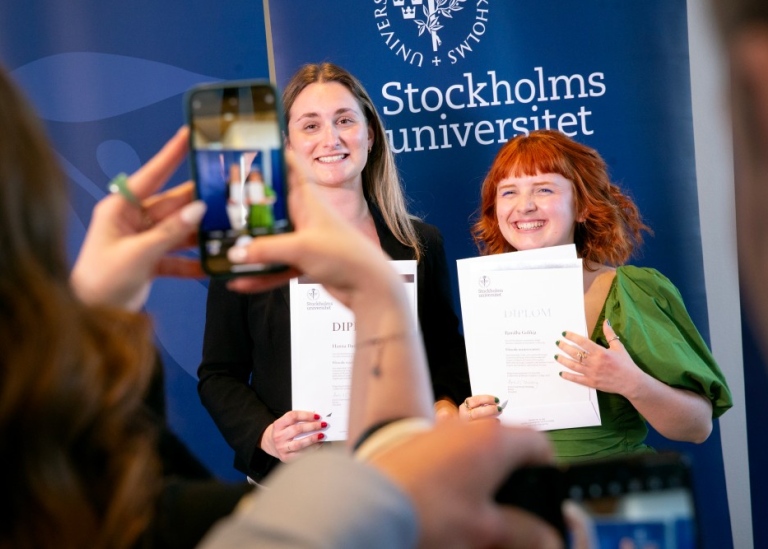 Två nöjda studenter fotas med examensbevisen i handen.