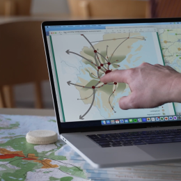 Finger pekar på laptopskärm som visar en karta med noder. Datorn står på en karta över Stockholm.