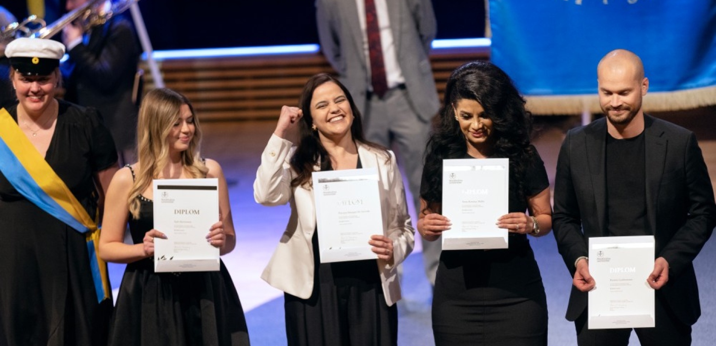Four master students om stage with diplomas in their hands.