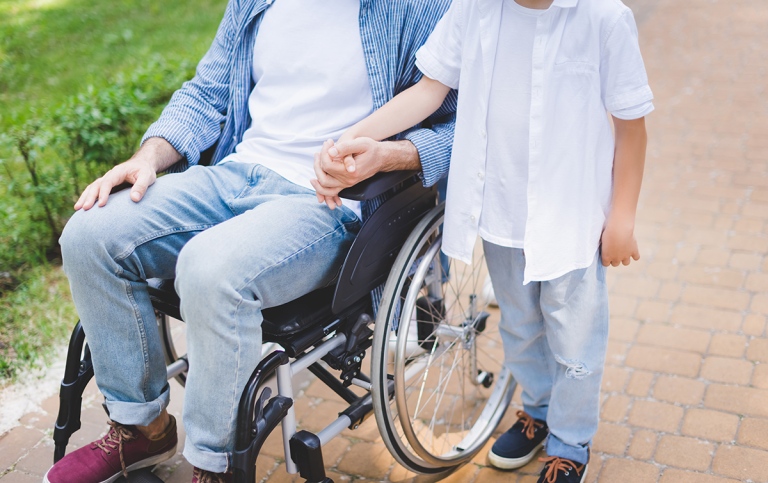 Son holding hands with disabled father in wheelchair