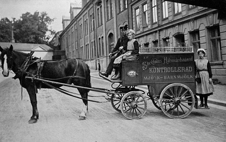 Svartvitt äldre foto av häst och mjölkvagn i stadsmiljö