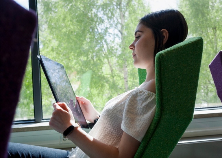 Kvinnlig student som sitter i grön fåtölj och tittar på en dator.
