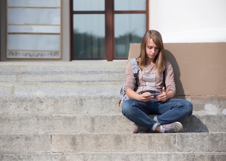 A lonely girl with a phone sits on the steps