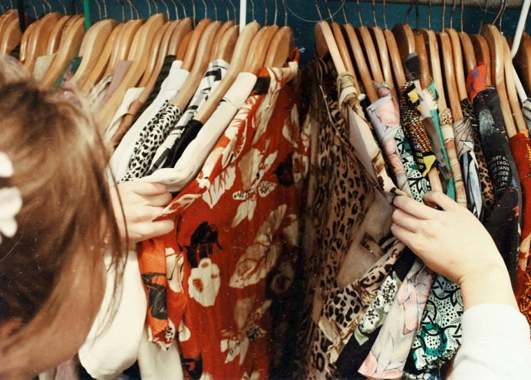The back of the head of a woman looking through clothes on a rack.