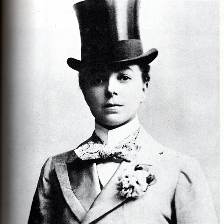Svartvit porträttbild på kvinna i manshatt och kostym. Taget i början av 1900-talet.