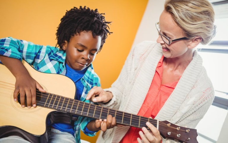 Lärare visar pojke hur ha kan spela på gitarren.