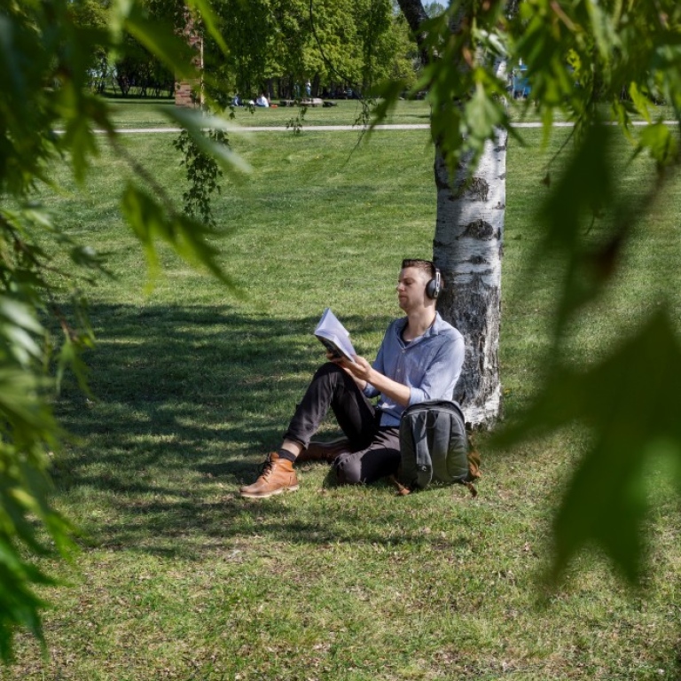 Student sitter under träd och läser