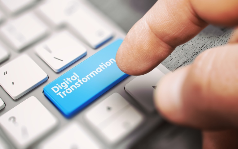 A hand above a computer keyboard where one key is blue and marked "Digital Transformation".