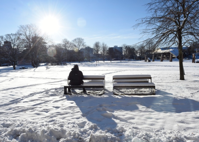 Student sitting on a bench in a wintery landscape.