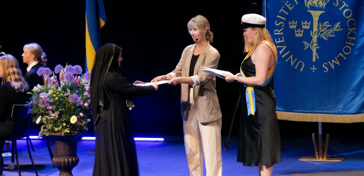 Student in black dress receiving her diploma at the conferment of master's degrees, May 2024.
