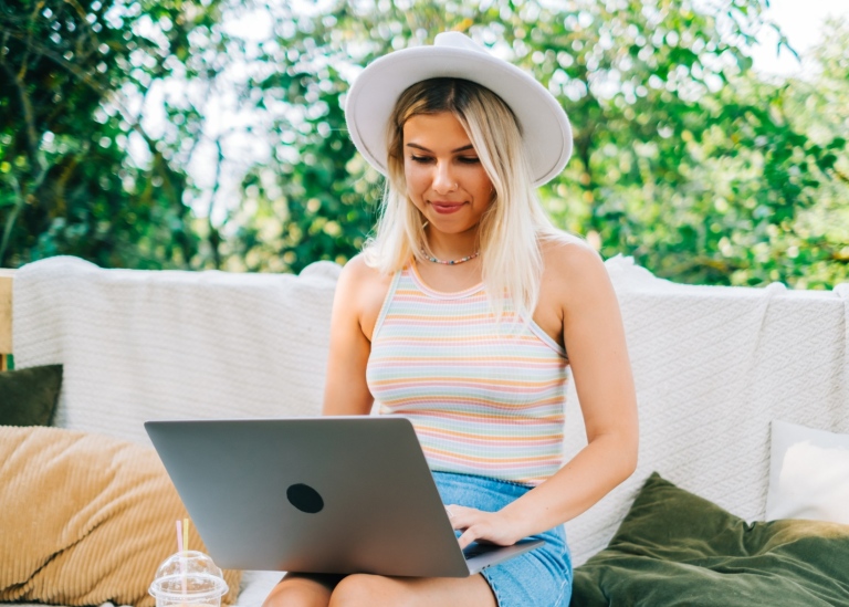 Ung sommarklädd kvinna sitter utomhus skriver på laptop.