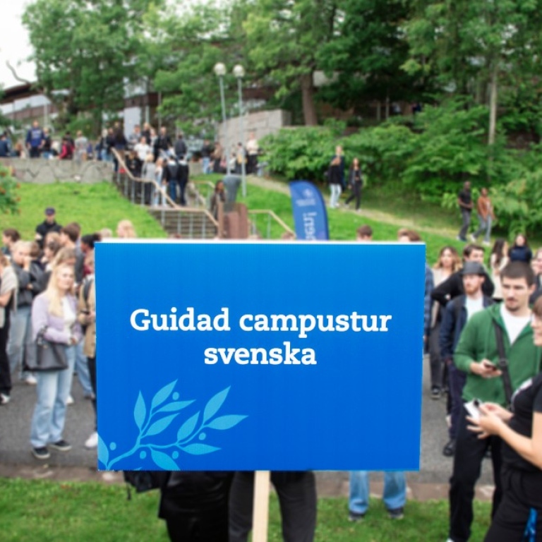Studenter på campus och blå skylt för guidad campustur