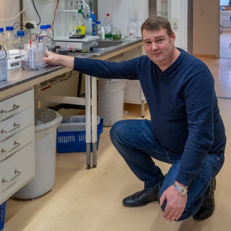 Claes kneeling infront of a workbench with full laboratory set up.