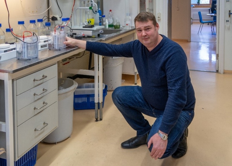 Claes kneeling infront of a workbench with full laboratory set up.