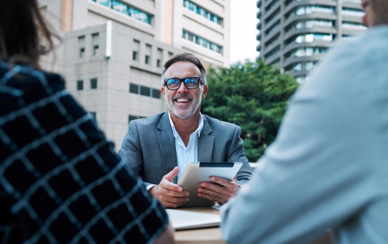 A smiling boss with a tablet, outside discussing with his collleagues.