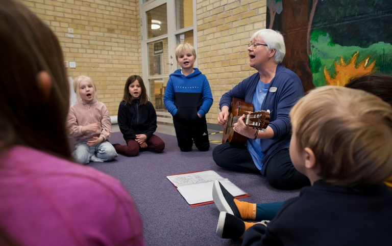 Lärare spelar gitarr och sjunger tillsammans med barn i förksoleklass. 