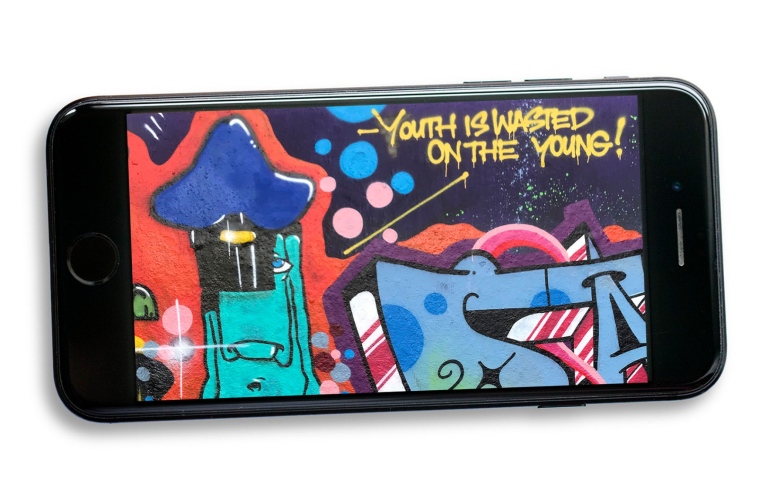Åldrande graffitiimålare håller sin unga identitet vid liv genom berättelser och bilder på sociala medier. Illustration: Malcolm Jacobson. Graffiti som visas på en mibilskärm. På bilden står texten: Youth is waisted on the young.